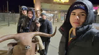 Five young men in winter coats posing next to a metal bull statue at night